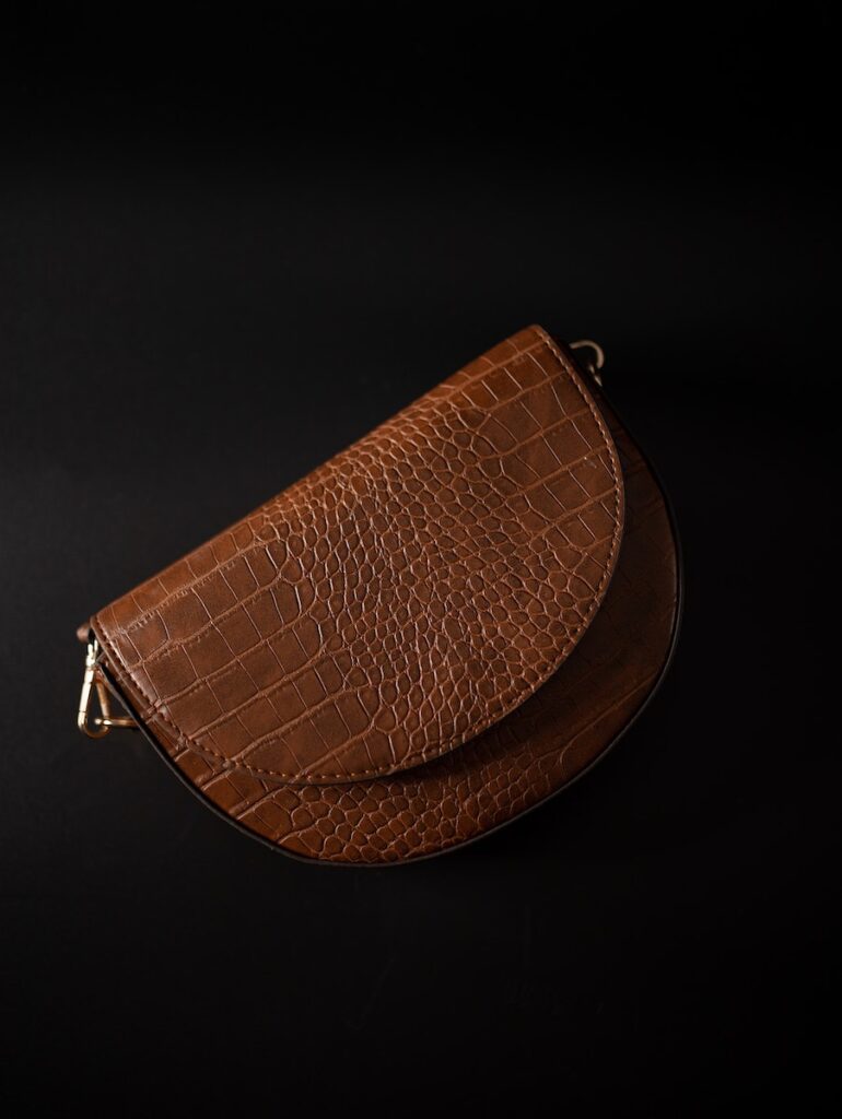 Top view classy brown leather purse of oval shape placed on black surface in studio